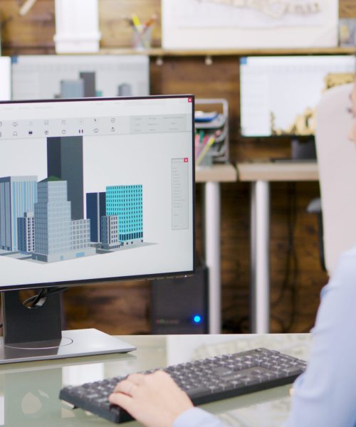 Female architect making 3d building models on computer Female architect making 3d building models on computer. Architect holding blueprint.